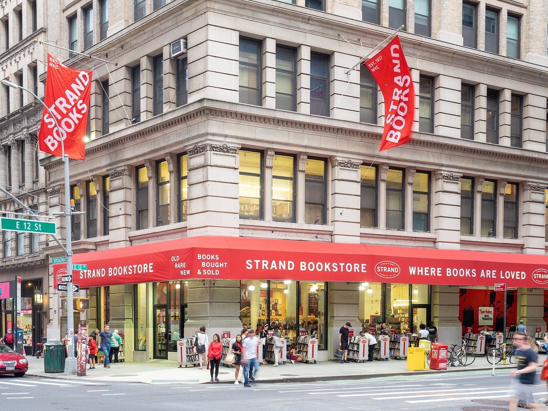Exterior da Livraria Strand com toldos vermelhos e pessoas passando em frente à vitrine