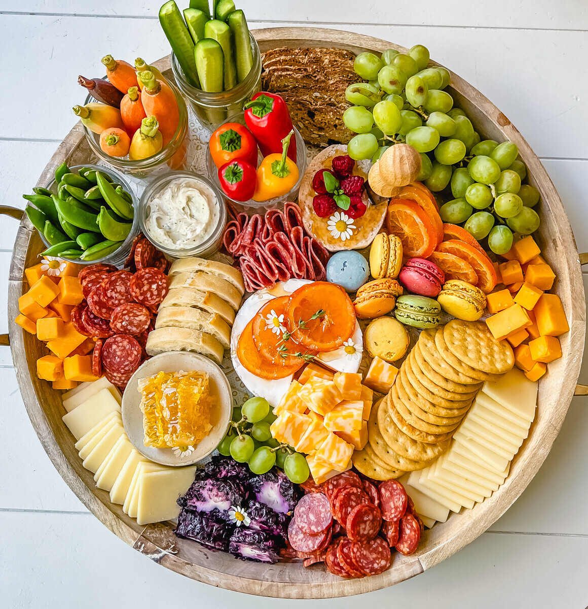 Round charcuterie board with meats, cheese, crackers, and other colorful snacks